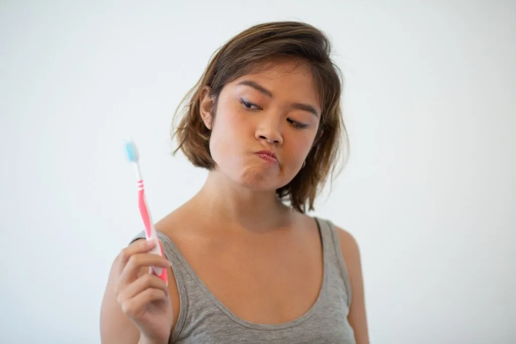 Doubtful pretty woman looking at toothbrush